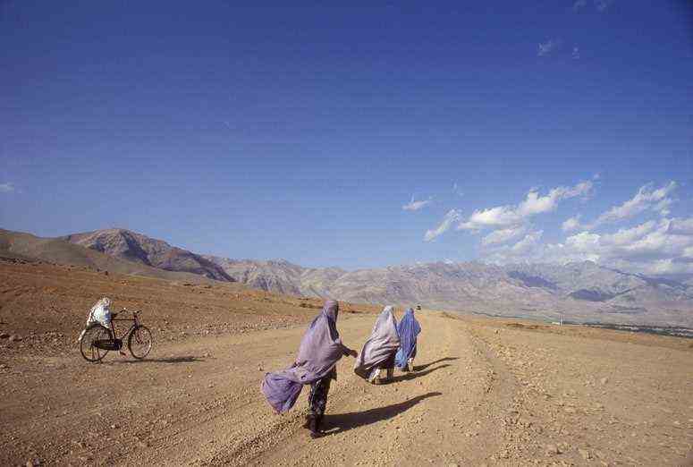 Drei Frauen gehen einen Feldweg in Richtung der Berge hinunter