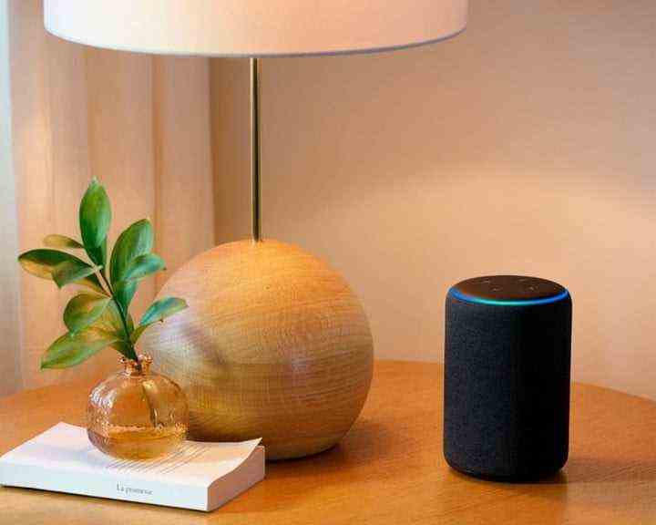 Amazon Echo auf einem Tisch neben einer Lampe und einem Buch.