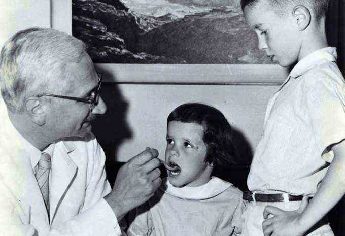 Albert Sabin gibt einem kleinen Kind den Polio-Impfstoff, während ein anderes Kind wartet
