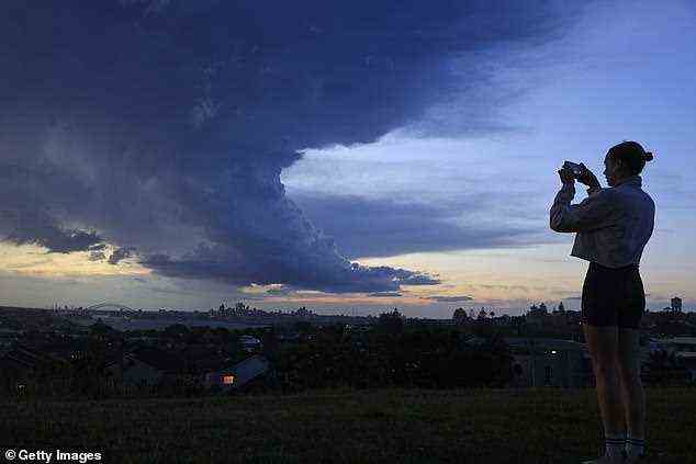 Eine Frau macht ein Foto von der Skyline der Stadt, während sich am Donnerstag Gewitterwolken über Sydney zusammenziehen