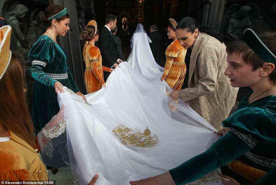 The bridal party, dressed in velvet green and orange gowns, could be seen carrying the lengthy train and veil of the gown (pictured)
