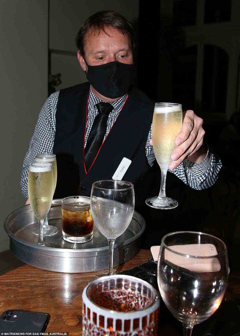 A server wearing a face mask places a glass of sparkling wine down on the table as the celebrations get underway