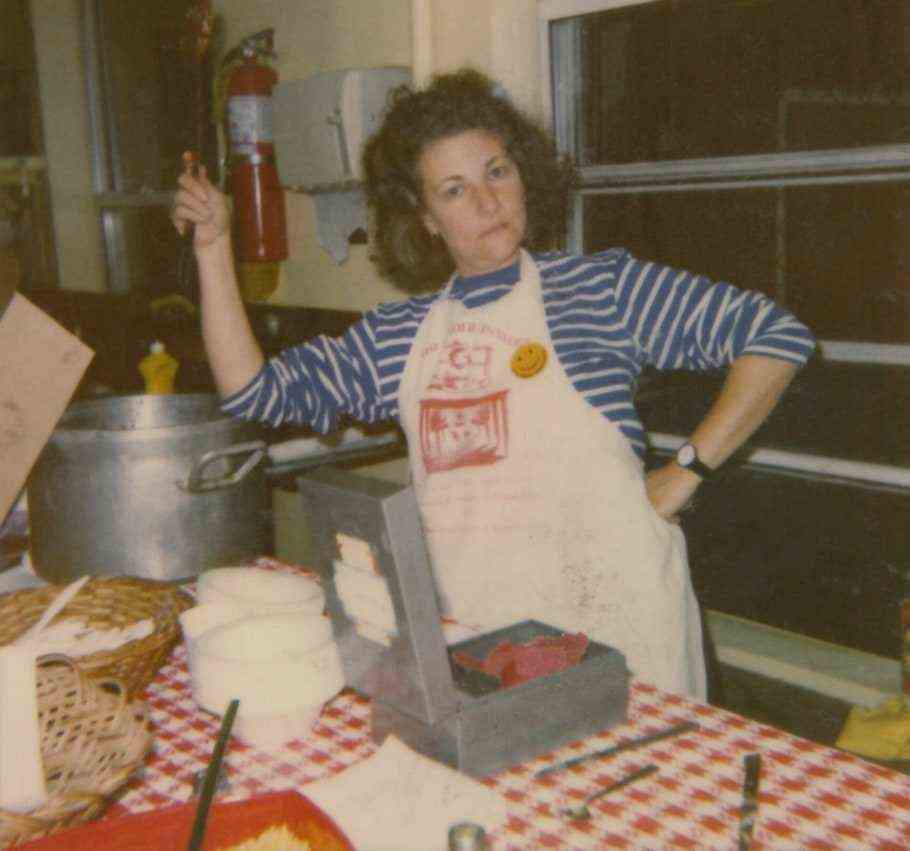 A woman poses wearing an apron in a kitchen.