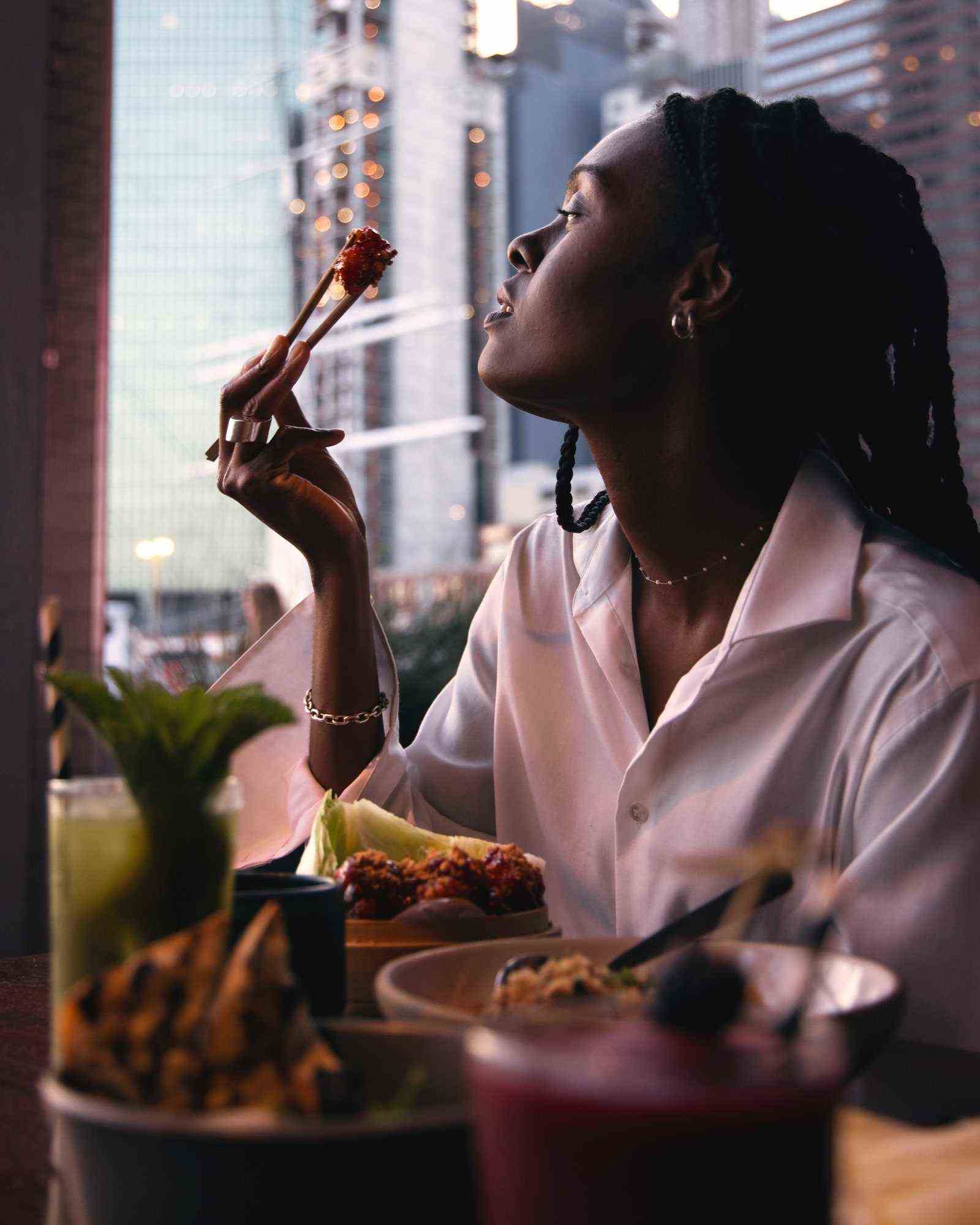 Eine Person schaut aus dem Fenster, während sie ein Stück Essen zwischen Stäbchen hält.