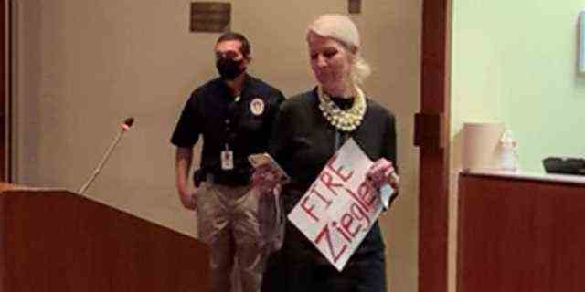 Eine Mutter aus Loudoun County, Virginia, betritt eine Schulausschusssitzung mit einem Schild mit der Aufschrift "Feuer Ziegler," 12. Oktober 2021.