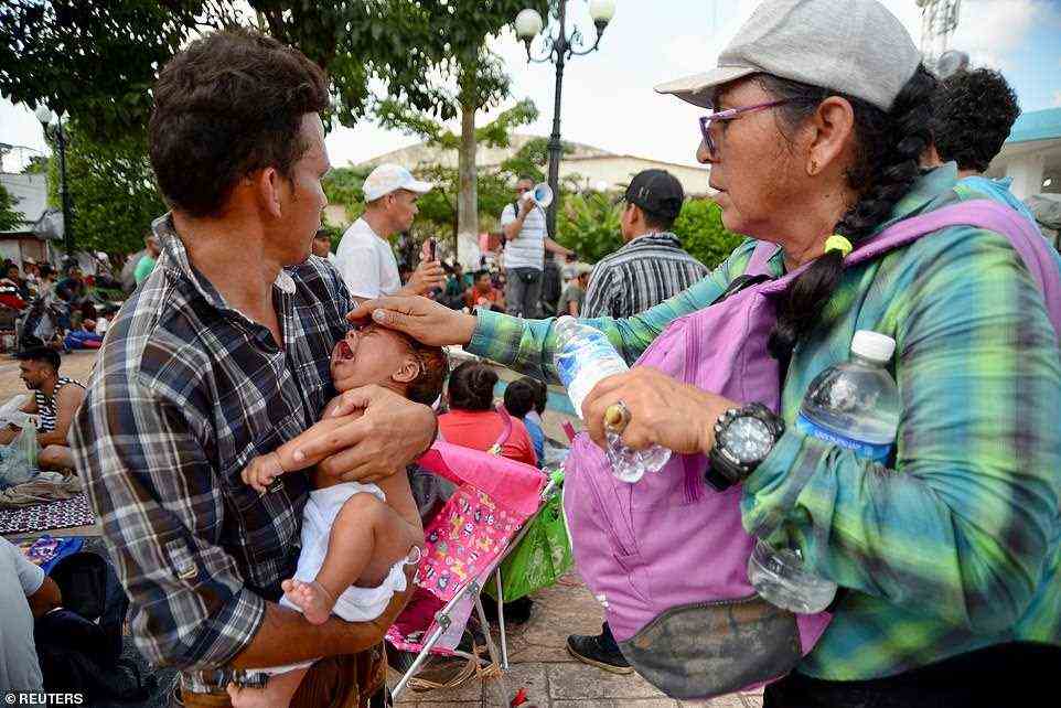 A woman pours water over the head of a baby as she rests along other migrants taking part in a caravan heading to Mexico City, in Escuintla, Mexico, on Thursday.