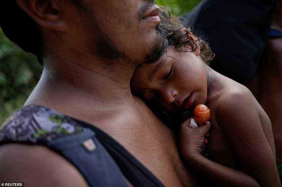 Alison, a four-year-old Honduran girl who is sick with fever, holds a lollypop as her father carries her