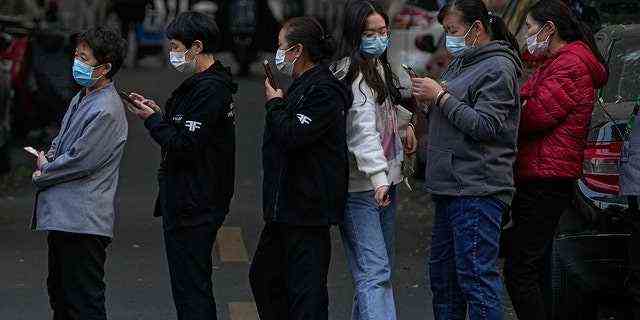 Eine Frau, die eine Gesichtsmaske trägt, um die Ausbreitung des Coronavirus einzudämmen, geht durch eine Reihe maskierter Frauen aus dem Dienstleistungssektor, die darauf warten, während eines Massentests in Peking am Freitag einen Tupfer für den COVID-19-Test zu erhalten, nachdem ein Anstieg des Coronavirus in der Hauptstadt und anderen Provinzen. 