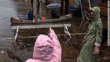 Eine Frau zeigt auf zwei Personen, die in einem Kanu in der Altstadt von Alexandria, Virginia, durch Hochwasser paddeln.