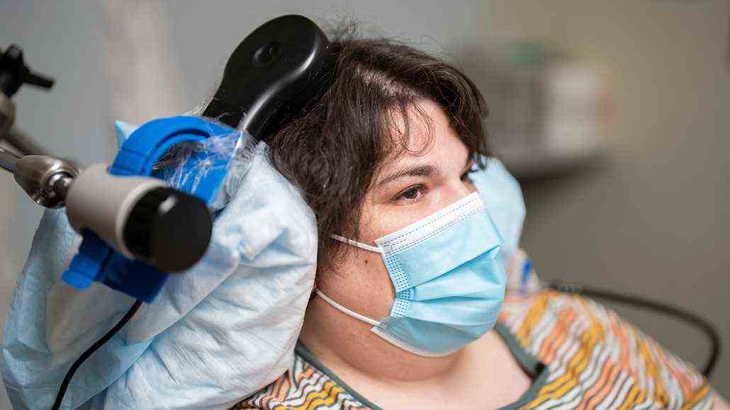 Frau, die eine Gesichtsmaske mit einem am Kopf angebrachten medizinischen Gerät trägt;  das Gerät misst die Gehirnaktivität