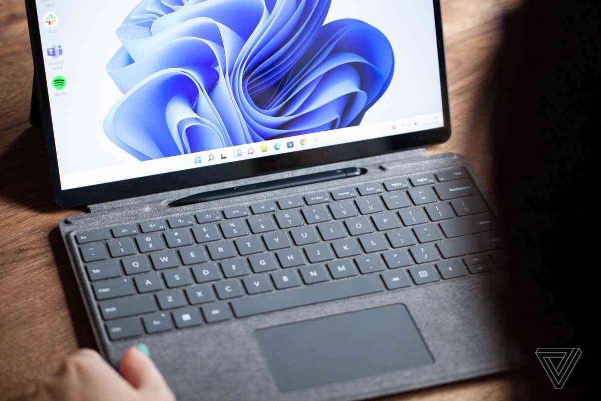 Das Surface Pro 8 wird aus der Nähe geöffnet, die Tastatur ist herausgezogen und der Stift sichtbar.  Der Bildschirm zeigt einen blauen Wirbel auf weißem Hintergrund.