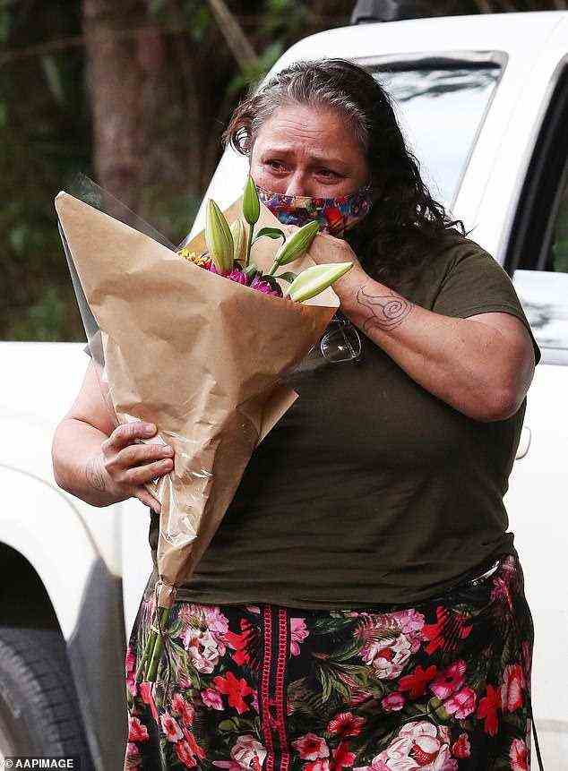 Ein Mitglied der Öffentlichkeit weint, während er einen Blumenstrauß vor dem Haus hält, in dem vierjährige Zwillingsmädchen nach einem Hausbrand starben