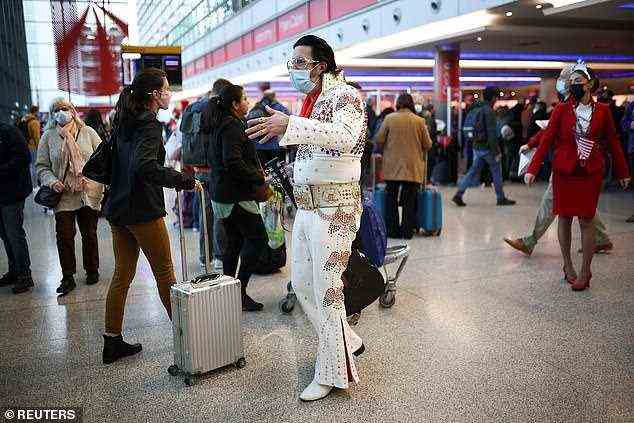 A performer dressed as Elvis Presley engages with travellers as they queue to check into Virgin Atlantic and Delta Air Lines flights at Heathrow Airport Terminal 3