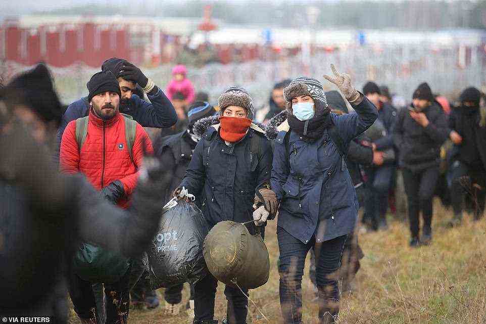 A group of migrants walks near a barbed wire fence while moving toward a makeshift camp on the Belarusian-Polish border