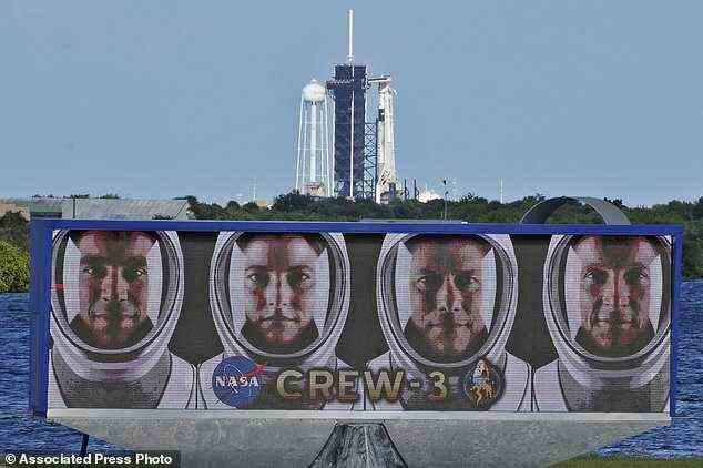 The official portraits of astronauts, from left, Raja Chari, Kayla Barron, Matthias Maurer, of Germany, and Tom Marshburn, are displayed at at the Kennedy Space Center in Cape Canaveral, Florida. A SpaceX Falcon 9 rocket with the Crew Dragon capsule attached sits on Launch Pad 39-A in the background