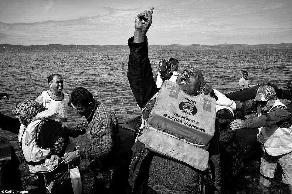 Pictured: A man gives thanks to Allah after landing on the Greek Island of Lesbos in a crowded rubber dinghy in 2015