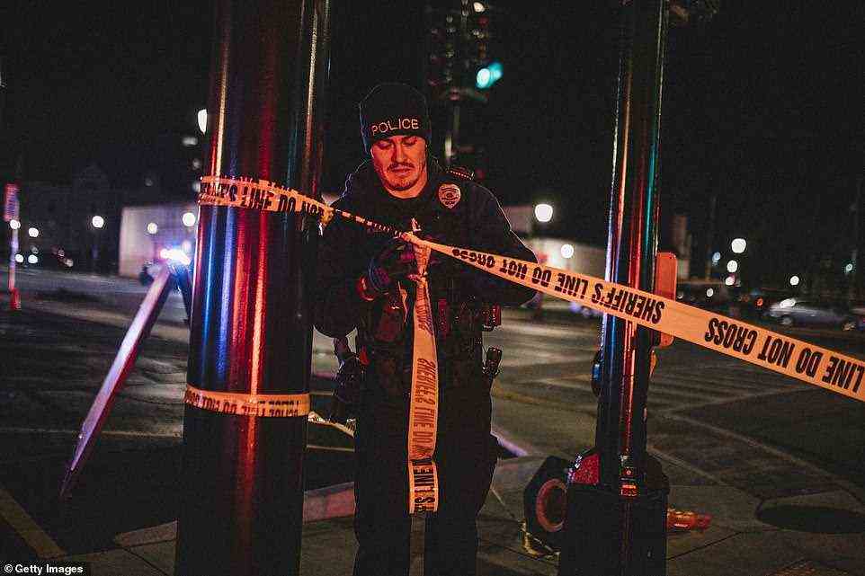 A police officer cordons off a crime scene near the area where a red SUV plowed into a crowd of paradegoers