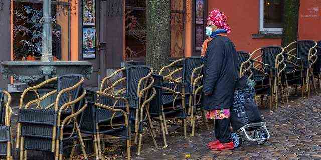 Eine Frau trägt eine Gesichtsmaske, um sich vor dem Coronavirus zu schützen, als sie am 17. November 2021 an einer leeren Terrasse im Viertel Marrolles in Brüssel, Belgien, vorbeikommt. 