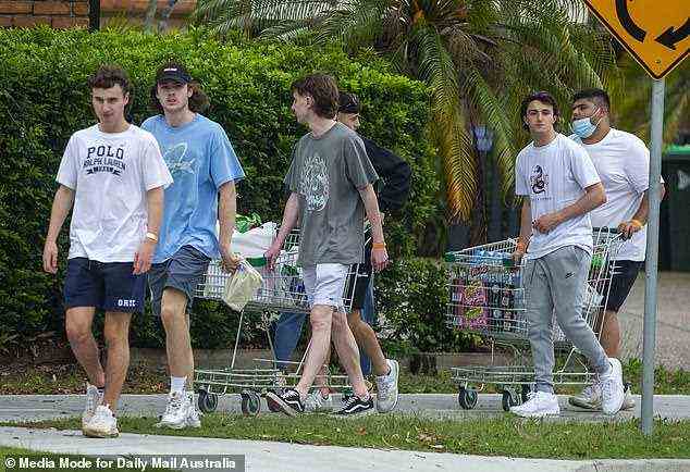 A group of mates are seen walking along the pavement in Byron Bay wheeling packed trolleys filled with drinks and supplies for the week ahead