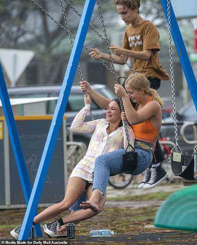 Hang on! Two friends are seen trying to coordinate riding a swing together as Schoolies kicks off
