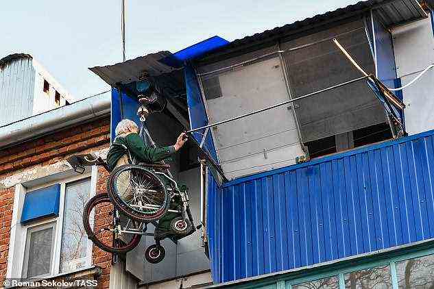 Herr Yudin erreicht sein Zuhause am oberen Ende des Aufzugs, indem er ein Tor auf seinem Balkon öffnet und seinen Körper und seinen Rollstuhl schwingt, um hineinzukommen