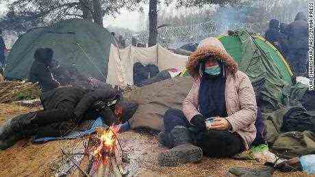 Erfrierende Migranten drängen sich in einem Zeltlager an der Grenze in der Nähe eines Lagerfeuers. 