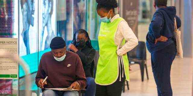 Menschen stehen am Freitag, den 26. November 2021 in einem Einkaufszentrum in Johannesburg, Südafrika, an, um sich impfen zu lassen Menschen in Gauteng, der bevölkerungsreichsten Provinz des Landes.  (AP-Foto/Denis Farrell)