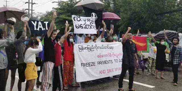 Protesters hold signs in Yangon on Oct. 30, 2021, calling for the freezing of revenues from oil and gas sales in Burma.