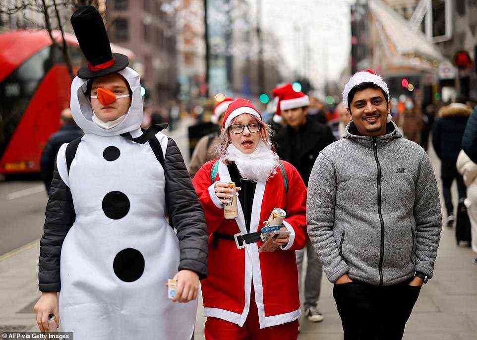 People dressed in Christmas-themed outfits including Santa hats walk along Oxford Street in London at about 12pm today