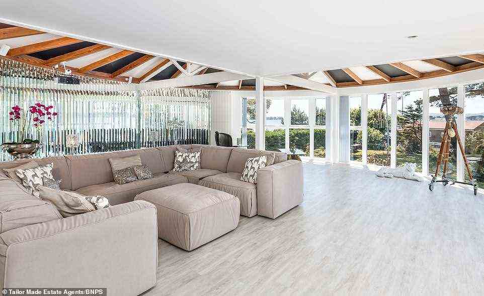 Dieser Loungebereich lässt viel natürliches Licht herein, mit raumhohen Glastüren, Holzbalken an der Decke und einem bequemen halbrunden Sofa in der Mitte