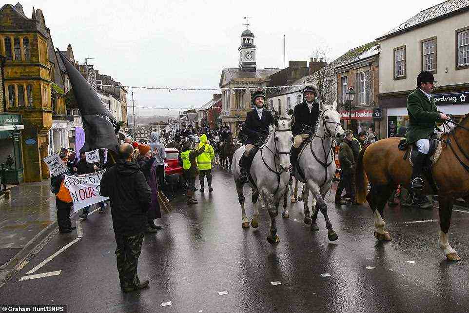 The Cotley Harriers ride their horses through the high street at Chard in Somerset on their annual Boxing Day hunt with locals and supporters cheering on despite a small handful of activists trying to ruin the day
