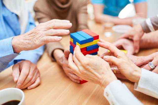 Gruppe Senioren mit Demenz baut im Pflegeheim einen Turm aus bunten Bauklötzen