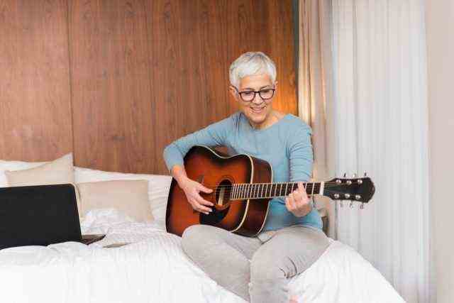 Reife Frau spielt Gitarre in ihrem Schlafzimmer, Freizeit und Hobbys