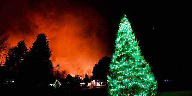 Ein Weihnachtsbaum ist immer noch mit Weihnachtsbeleuchtung beleuchtet, während am 30. Dezember 2021 in Louisville, Colorado, im Hintergrund Feuer wüten. 