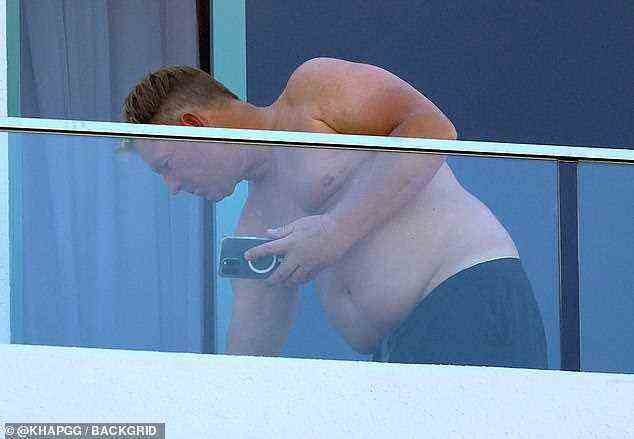 Abgelenkt werden: Shane hielt sein Telefon fest, beugte sich dann vor und inspizierte etwas auf seinem Hotelbalkon
