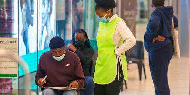 Menschen stehen Schlange, um sich am 26. November 2021 in einem Einkaufszentrum in Johannesburg, Südafrika, impfen zu lassen. (AP Photo/Denis Farrell)