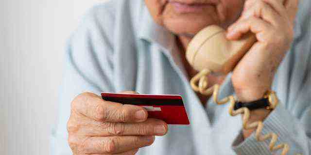 Frau, die Telefon benutzt, während sie Kreditkarte hält.