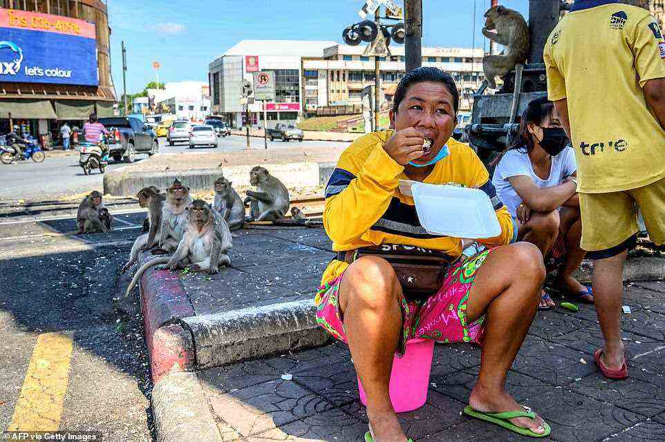 Locals eating on the street in June 2020 are watched over by longtailed macaques which have been left hungry after tourists vanished