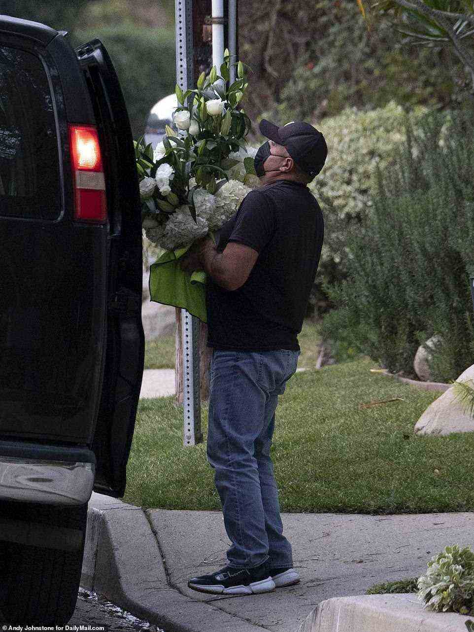 A man is seen carrying a large arrangement of flowers that appear to be for the private funeral service outside the couple's home