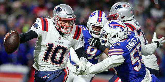 New England Patriots-Quarterback Mac Jones (10) läuft den Ball unter dem Druck von Jerry Hughes (55), dem defensiven Ende von Buffalo Bills, während der ersten Hälfte eines NFL-Wild-Card-Playoff-Fußballspiels, Samstag, 15. Januar 2022, im Orchard Park. NY