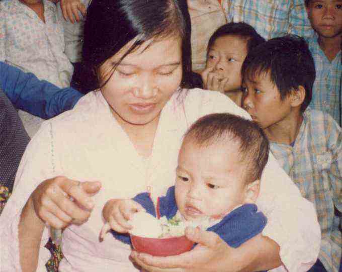 Foto einer Vietnamesin, die ein Baby hält und Reis aus einer Schüssel isst