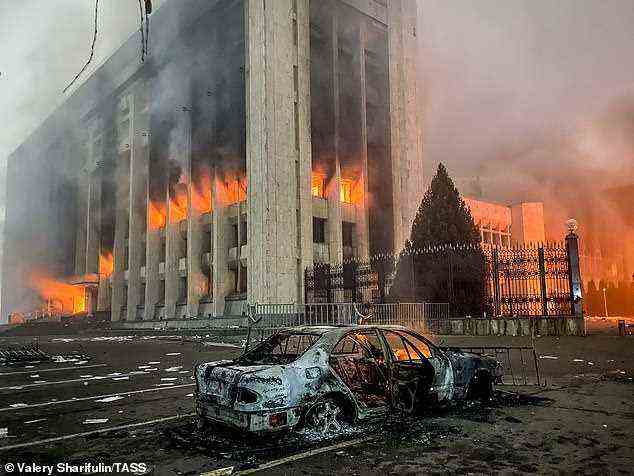 Ein verbranntes Auto wird vom Bürgermeisteramt in Flammen gesehen.  In ganz Kasachstan breiten sich Proteste gegen die steigenden Treibstoffpreise aus;  Demonstranten brachen in das Büro des Bürgermeisters von Almaty ein und zündeten es an