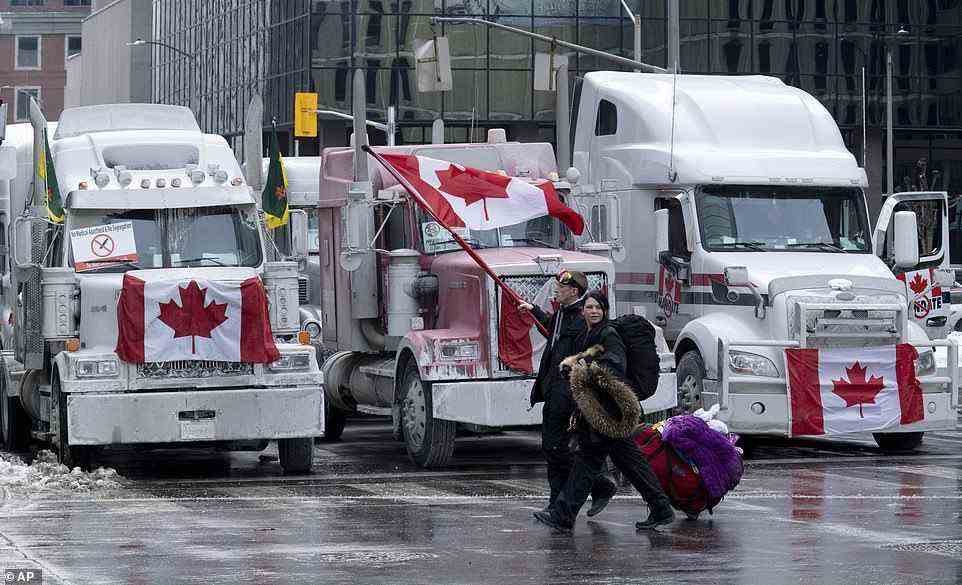 Protesters walk with bags past trucks parked on Downtown streets in Ottawa on Wednesday. The demonstrations have been going on for nearly a week