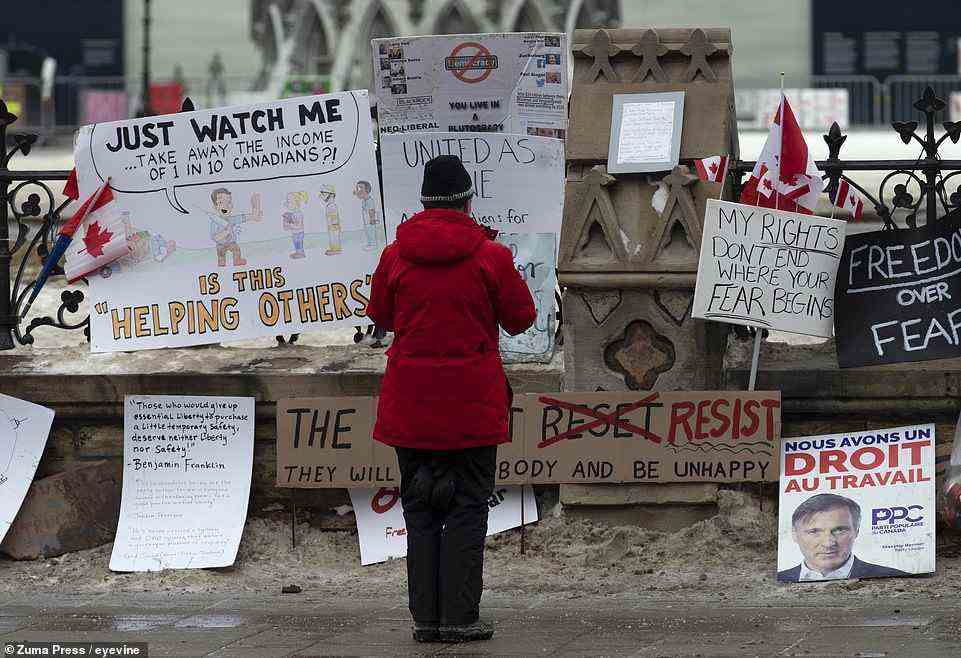 A woman stops to take a photo of signs attached to the fence around Parliament as a trucker protest continues