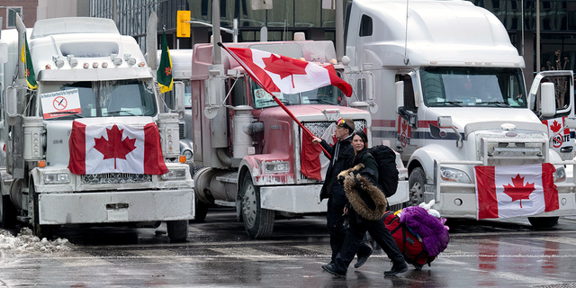 Demonstranten gehen am Mittwoch, den 2. Februar 2022, in Ottawa, Ontario, mit Taschen an Lastwagen vorbei, die auf den Straßen der Innenstadt geparkt sind.  (Adrian Wyld/The Canadian Press über AP)