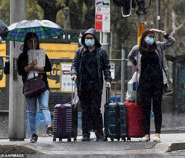 Maskierte Fußgänger schützen sich im Geschäftsviertel von Sydney vor dem Regen.  Bis zum 28. Februar müssen in allen öffentlichen Innenräumen, einschließlich Supermärkten, Pubs und Cafés, Masken getragen werden