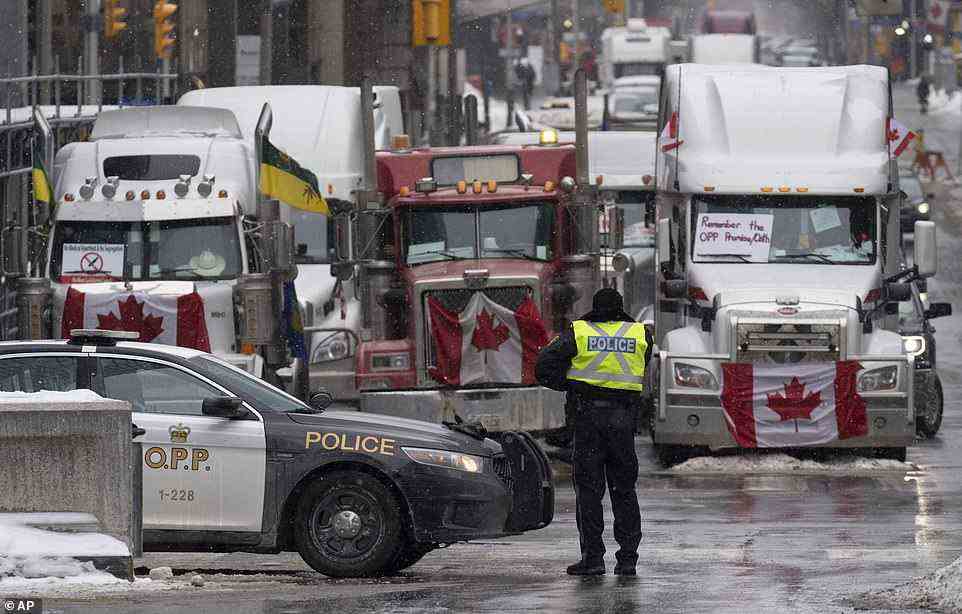 Daily demonstrations, going on day 11, began as a protest against vaccine requirements for truckers who enter the country by land. Pictured: Police man a barricade in front of vehicles parked as part of the trucker protest on Tuesday in Ottawa