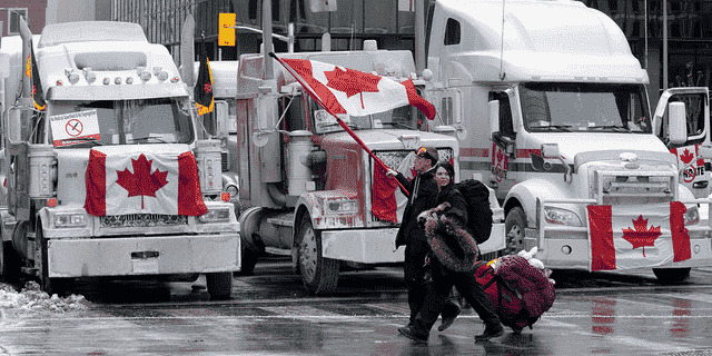Demonstranten gehen am Mittwoch, den 2. Februar 2022, in Ottawa, Ontario, mit Taschen an Lastwagen vorbei, die auf den Straßen der Innenstadt geparkt sind.  Tausende Demonstranten, die gegen Impfvorschriften und andere COVID-19-Beschränkungen protestierten, kamen in die Hauptstadt und blockierten absichtlich den Verkehr rund um den Parliament Hill. 