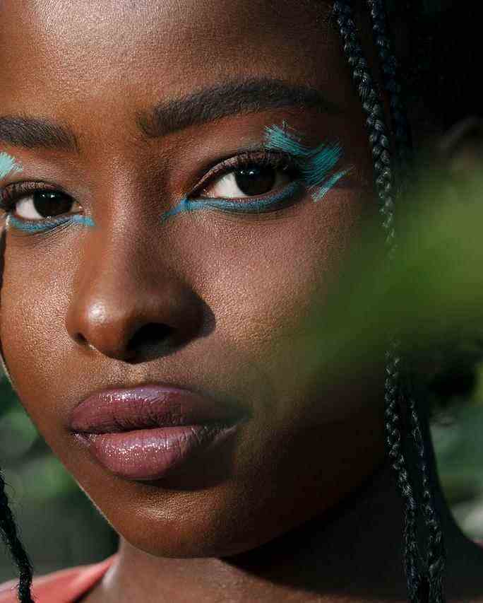 Close-up portrait of Amanda Gorman for Allure Magazine. She wears painterly light blue eye shadow and darker blue eyeliner on the bottom lashline paired with a neutral lipstick. Two small braids frame her face. 