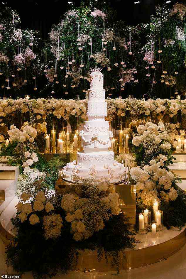 Haben ihren Kuchen und essen ihn auch!  Eine hoch aufragende, mehrstöckige Hochzeitstorte, umgeben von Blumen und brennenden Kerzen, die für ein großartiges Herzstück geschaffen wurden